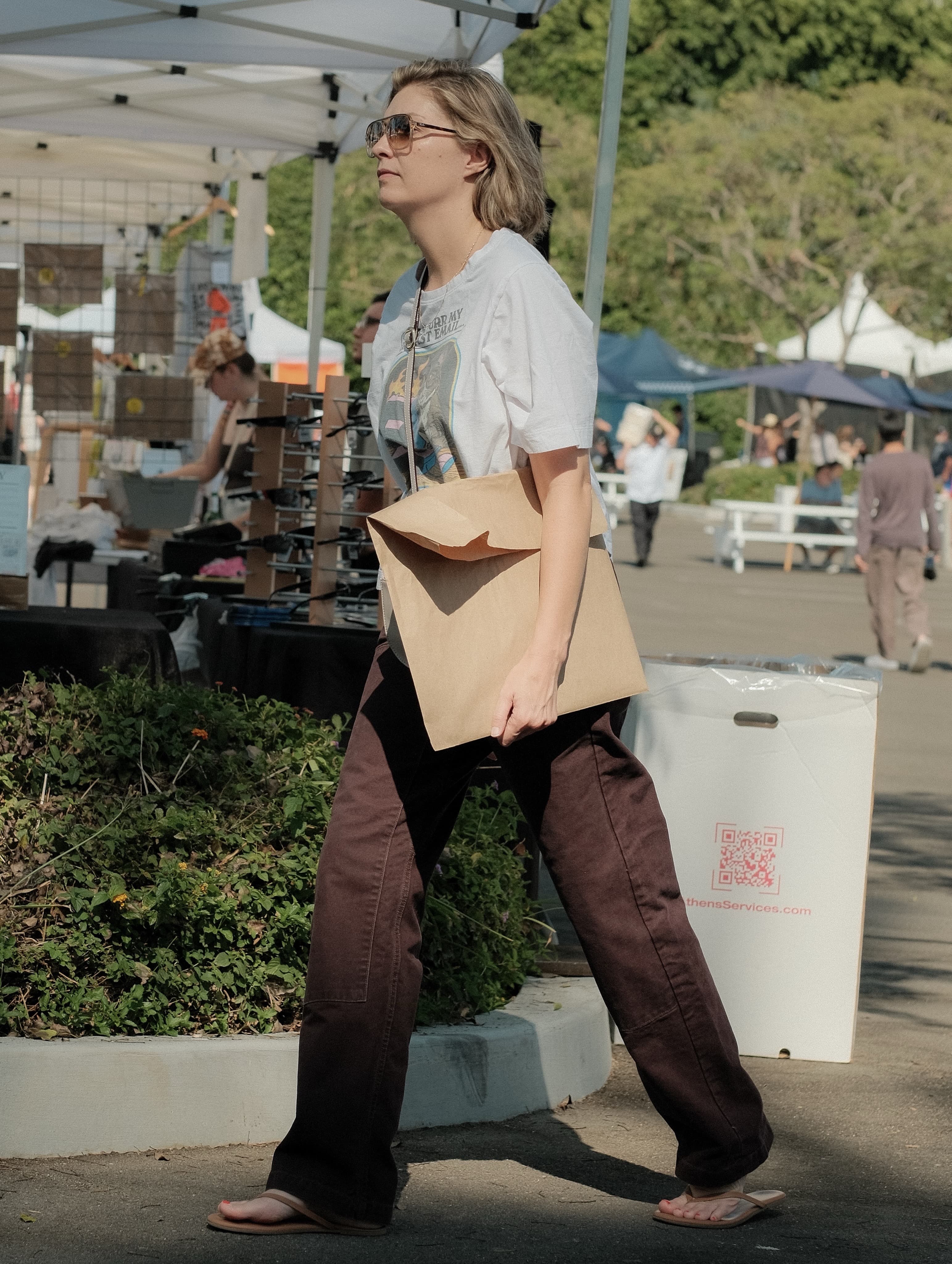 White graphic tee, wide maroon trousers, a kraft paper crossbody bag, at Spinning Sunset