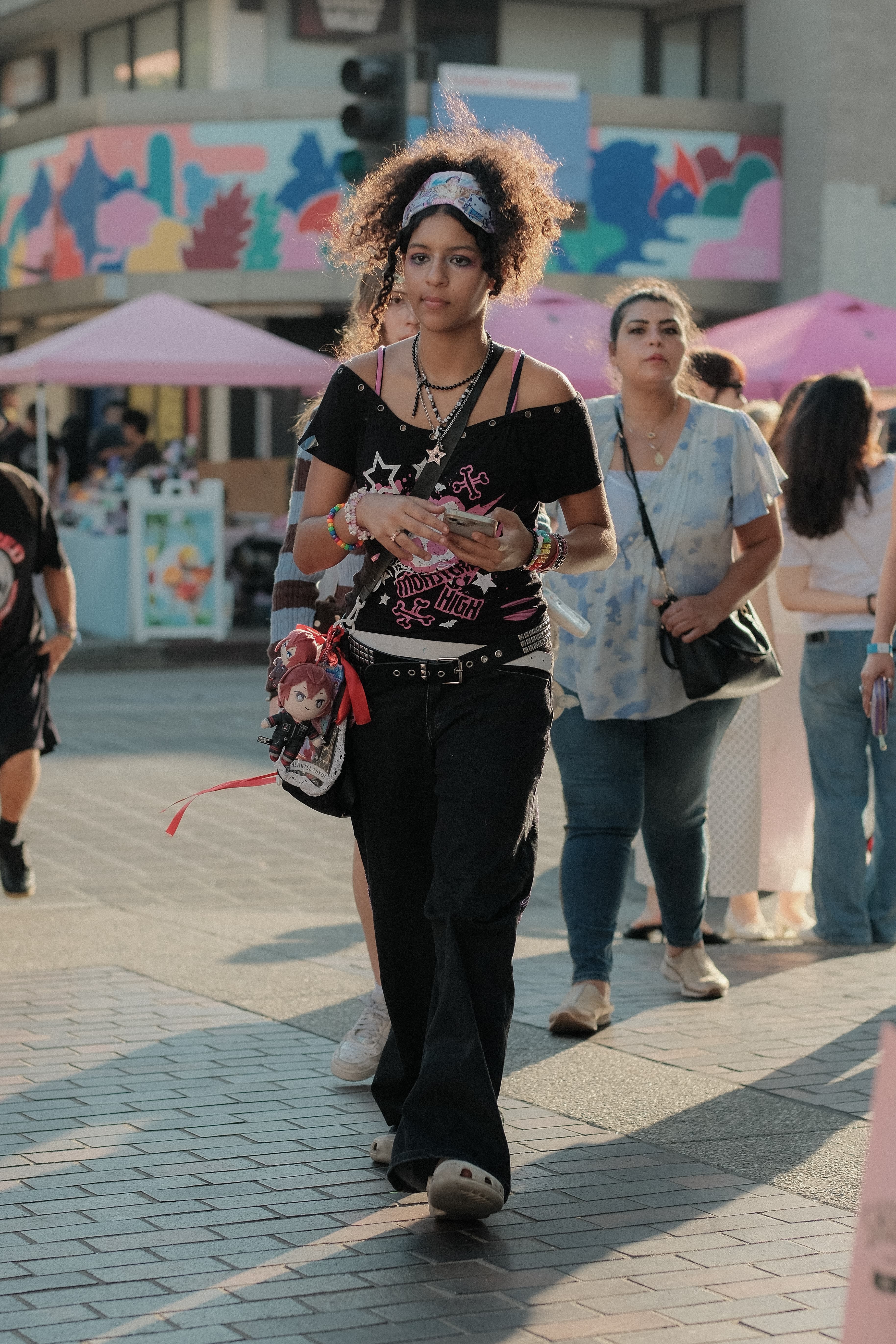 Off-shoulder graphic tee, baggy black jeans, charm-covered crossbody