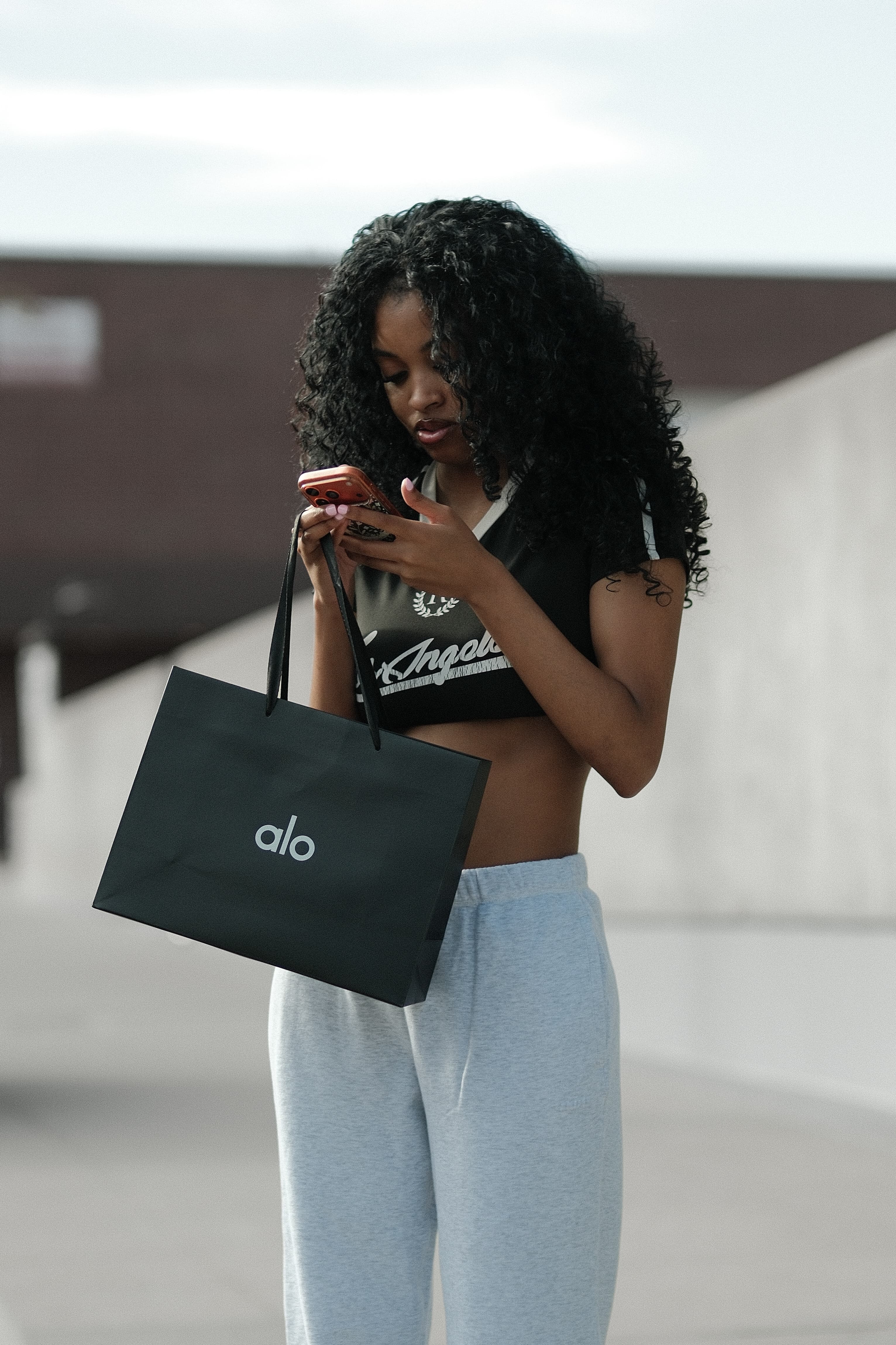 Cropped varsity tee, grey sweatpants, shopping bag in hand